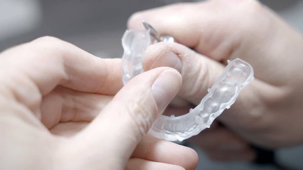 Techniker führt die Feinbearbeitung einer transparenten Knirscherschiene (Aufbissschiene) aus Kunststoff durch. Präzise Schienentherapie aus dem CCDE Dentallabor in Mönchengladbach.