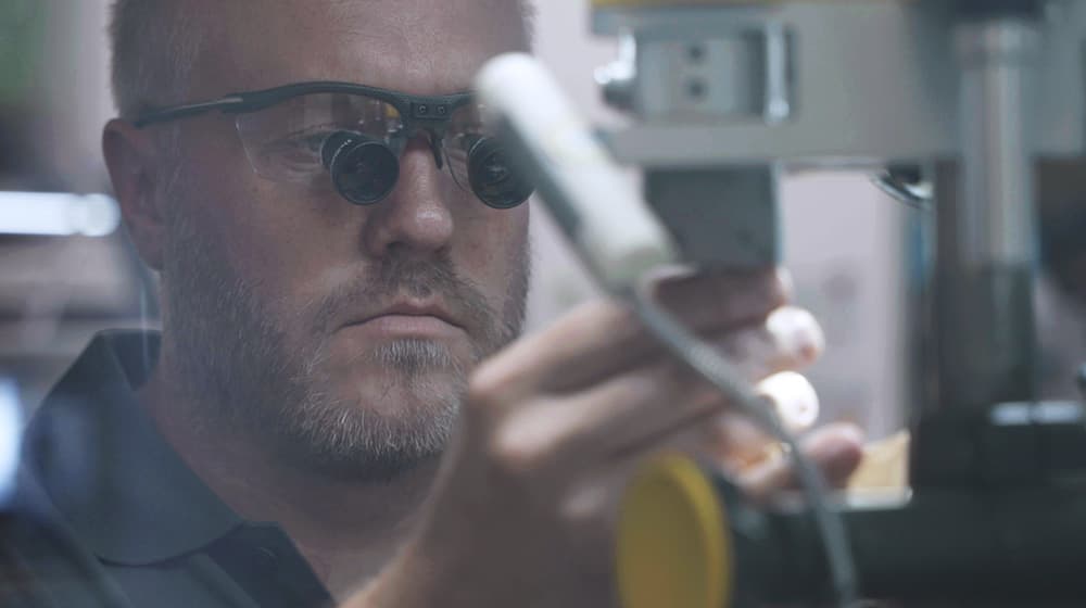 Erfahrener Zahntechniker mit Lupenbrille konzentriert sich auf Präzisionsarbeit an einem Dentalprodukt. Hochwertige Handwerkskunst Made in Germany von CCDE Mönchengladbach.
